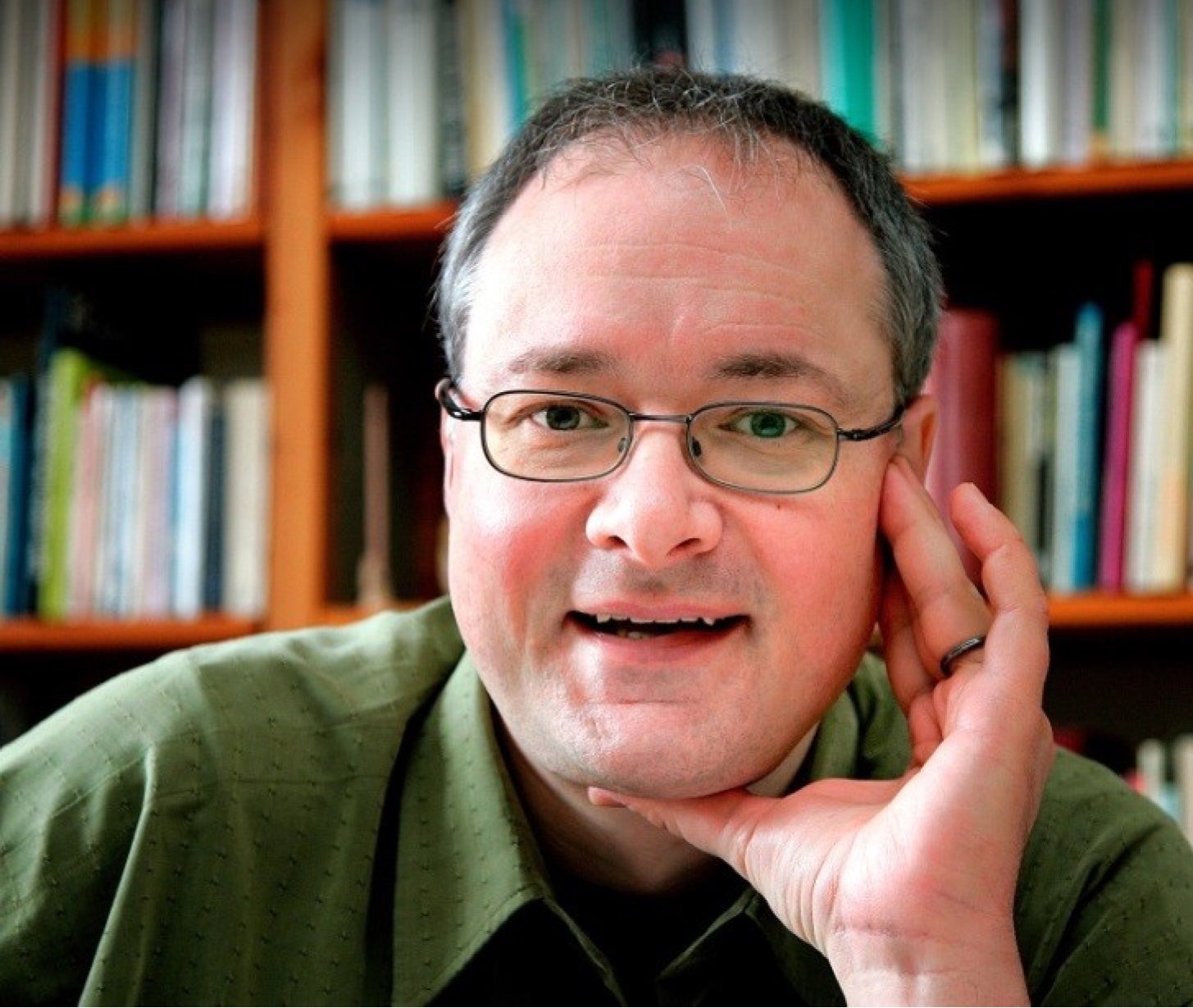 Headshot image of Jo Hecker smiling with his hand up to his face.