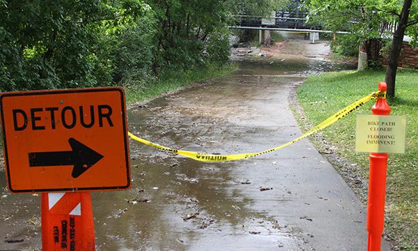 A detour sign and a caution tape block the bike path due to imminent flooding of the Boulder Creek.