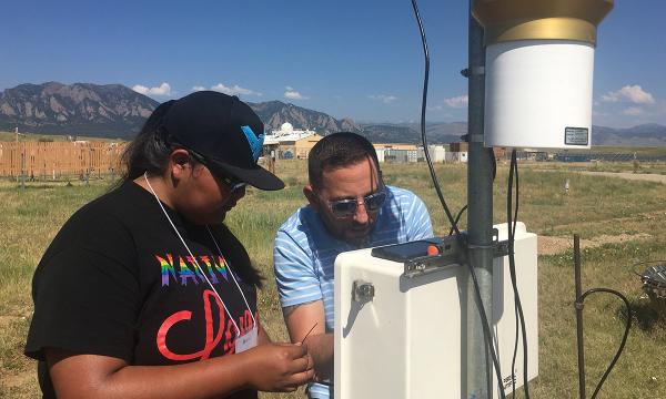 Student and mentor work together to install an instrument that measures wind speeds out in a field