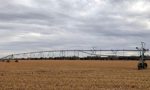 A center-pivot irrigation system in a brown field against a cloudy sky